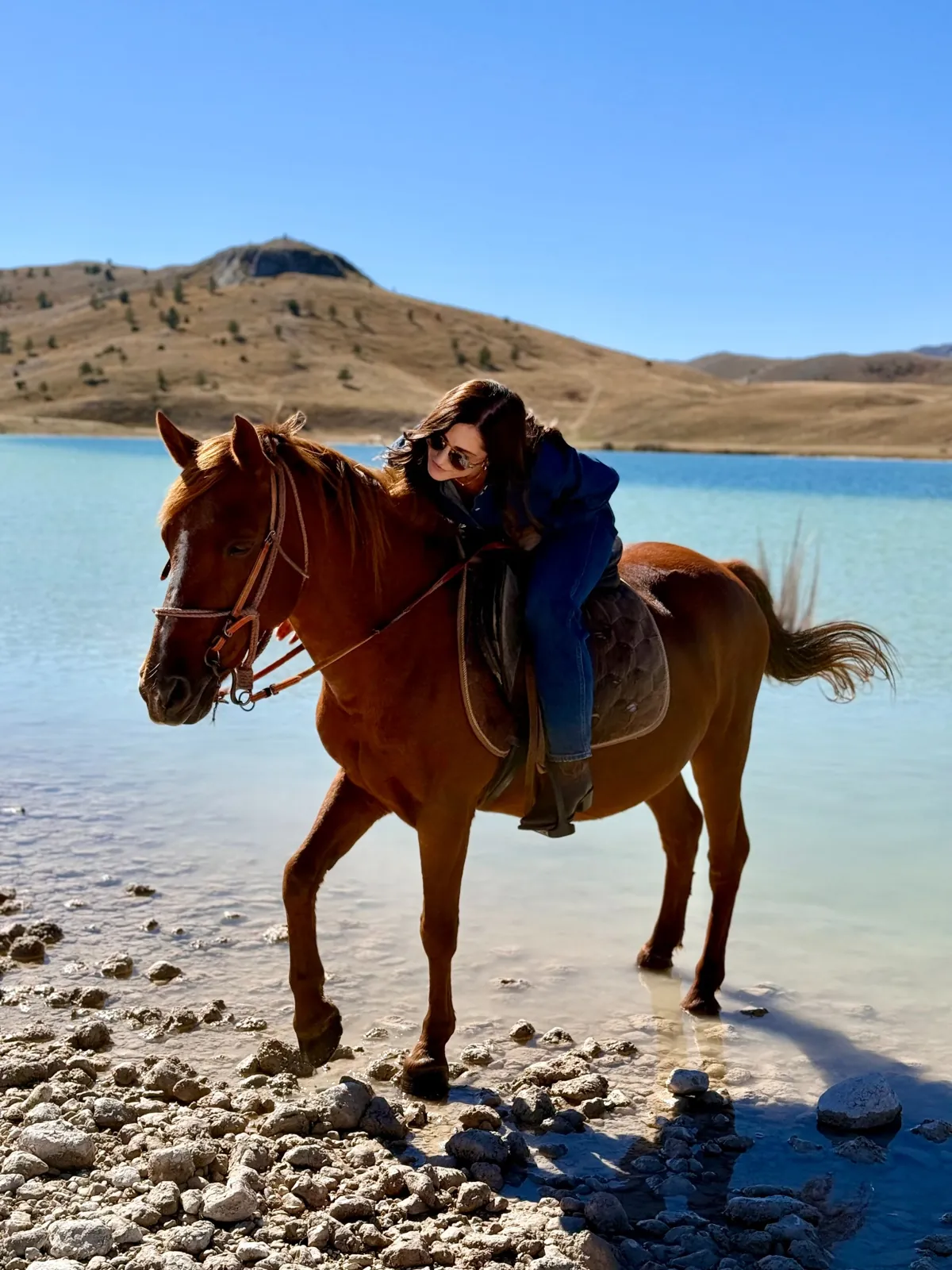 Guest on a chestnut horse at the edge of a turquoise lake