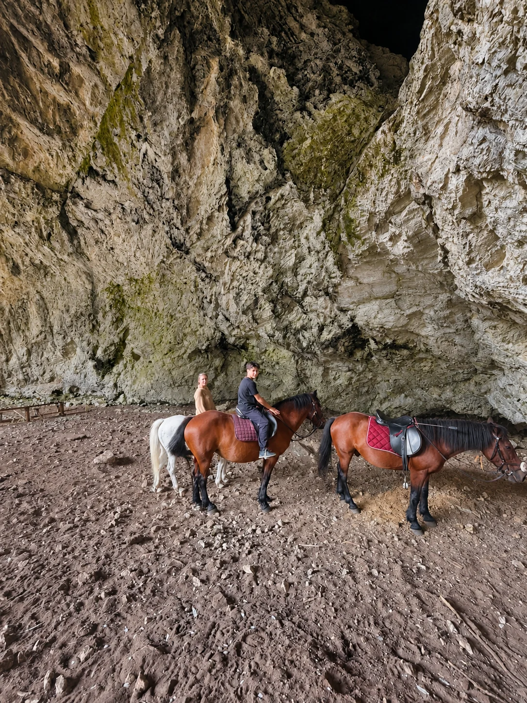 Riders and horses beside the towering rock walls of Đurova Cave