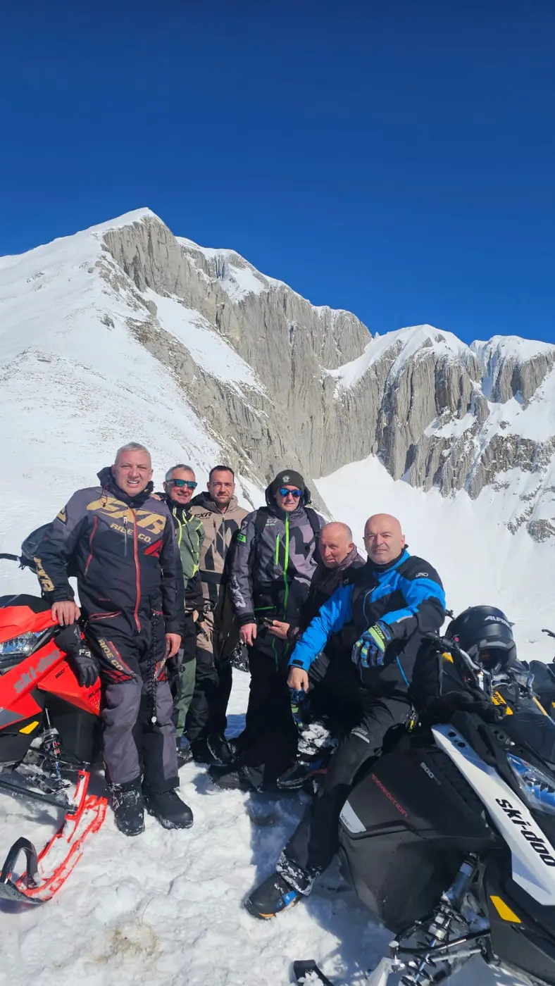 Snowmobile riders posing beneath the rocky winter cliffs of Durmitor